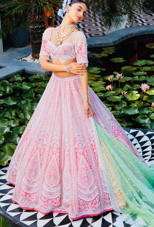 Woman in a traditional pink and green embroidered outfit standing in a garden with lotus flowers.