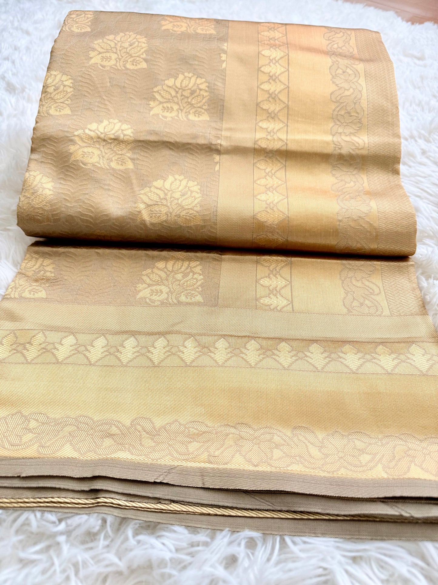 Beige saree with gold patterns on a white surface