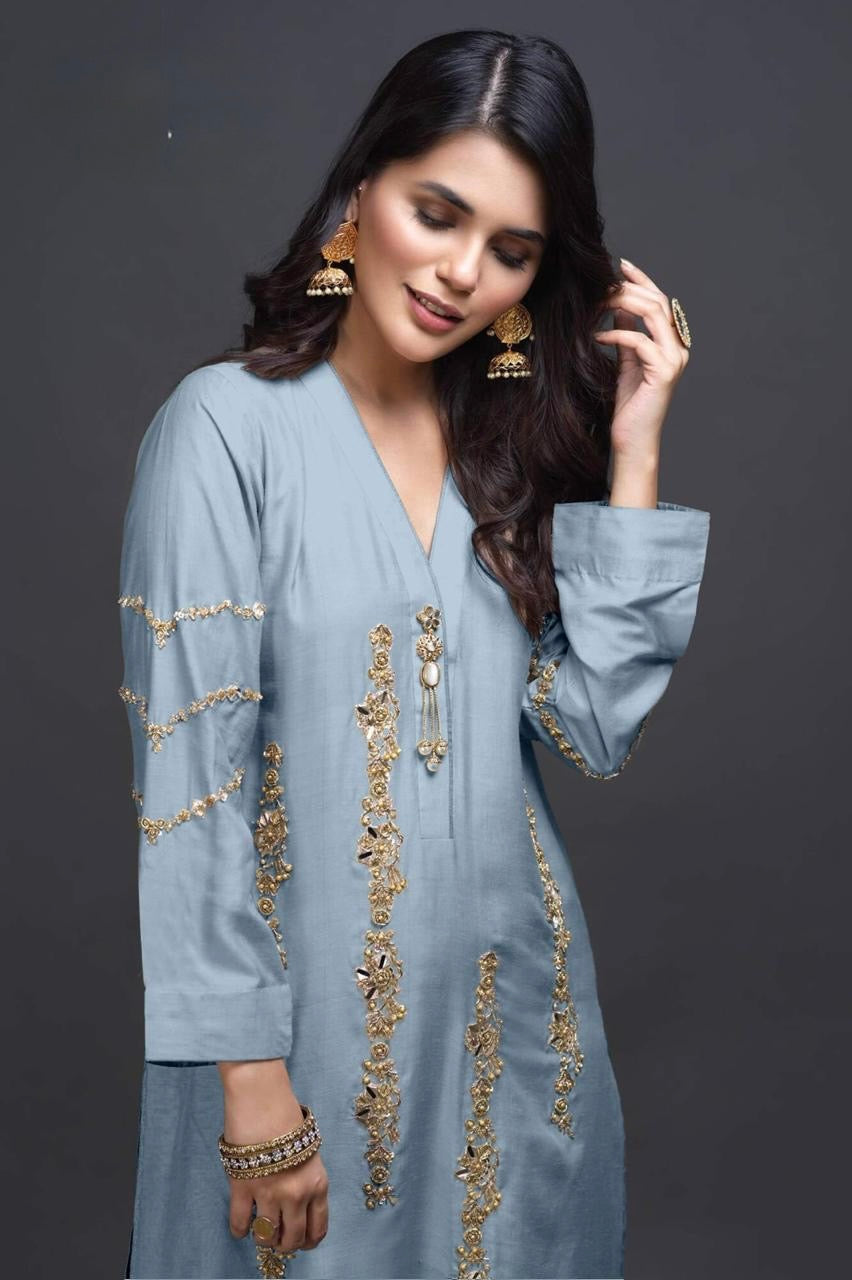 Woman wearing a light blue outfit with gold embroidery against a dark background