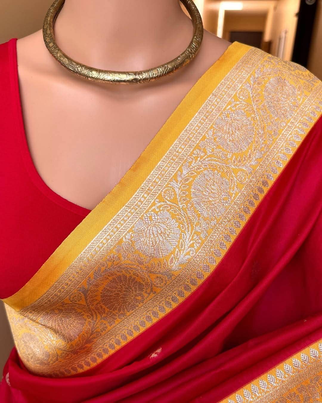 Red saree with a yellow border featuring intricate patterns on a mannequin.