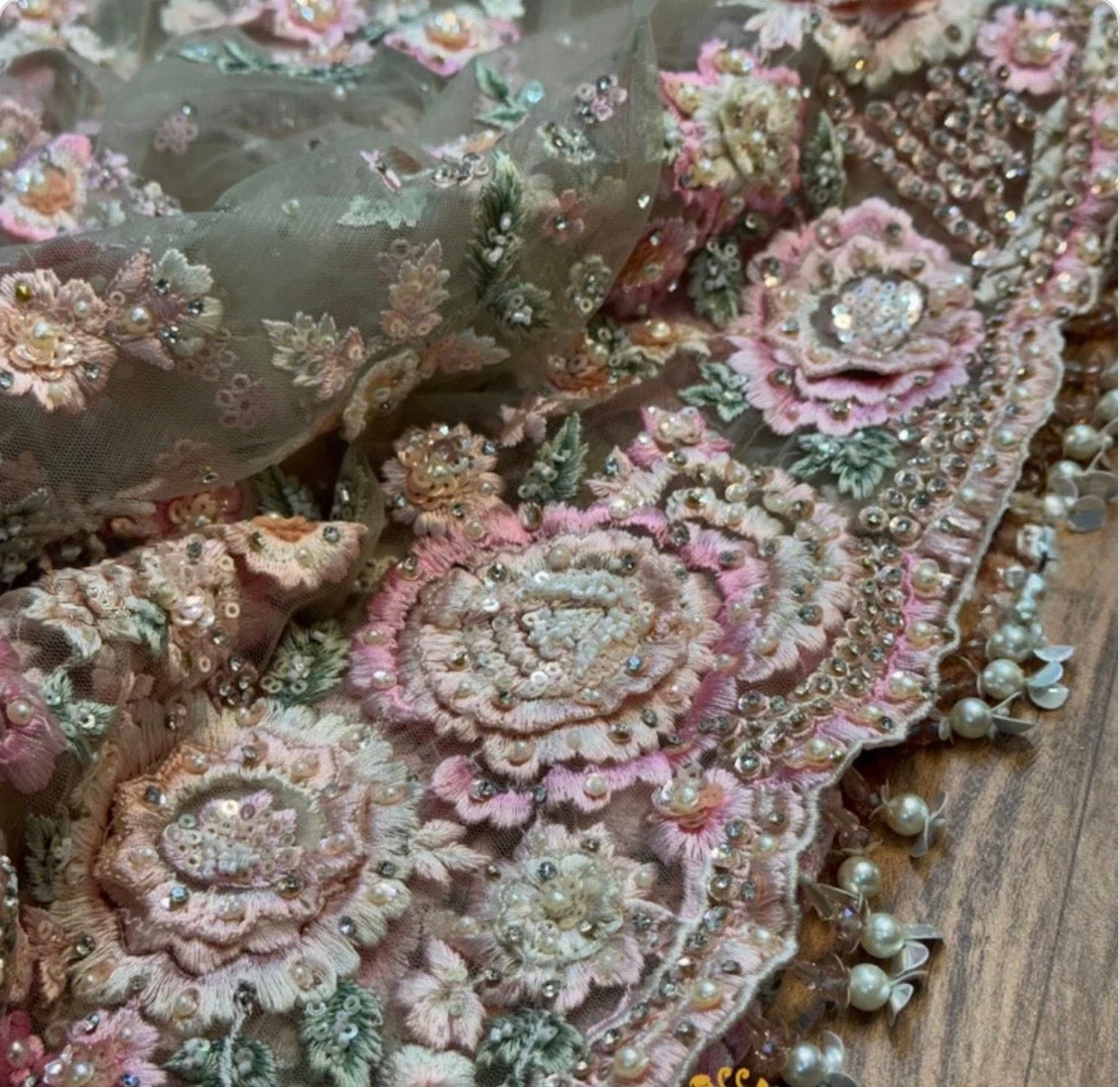Close-up of decorative fabric with floral patterns and beads on a wooden surface