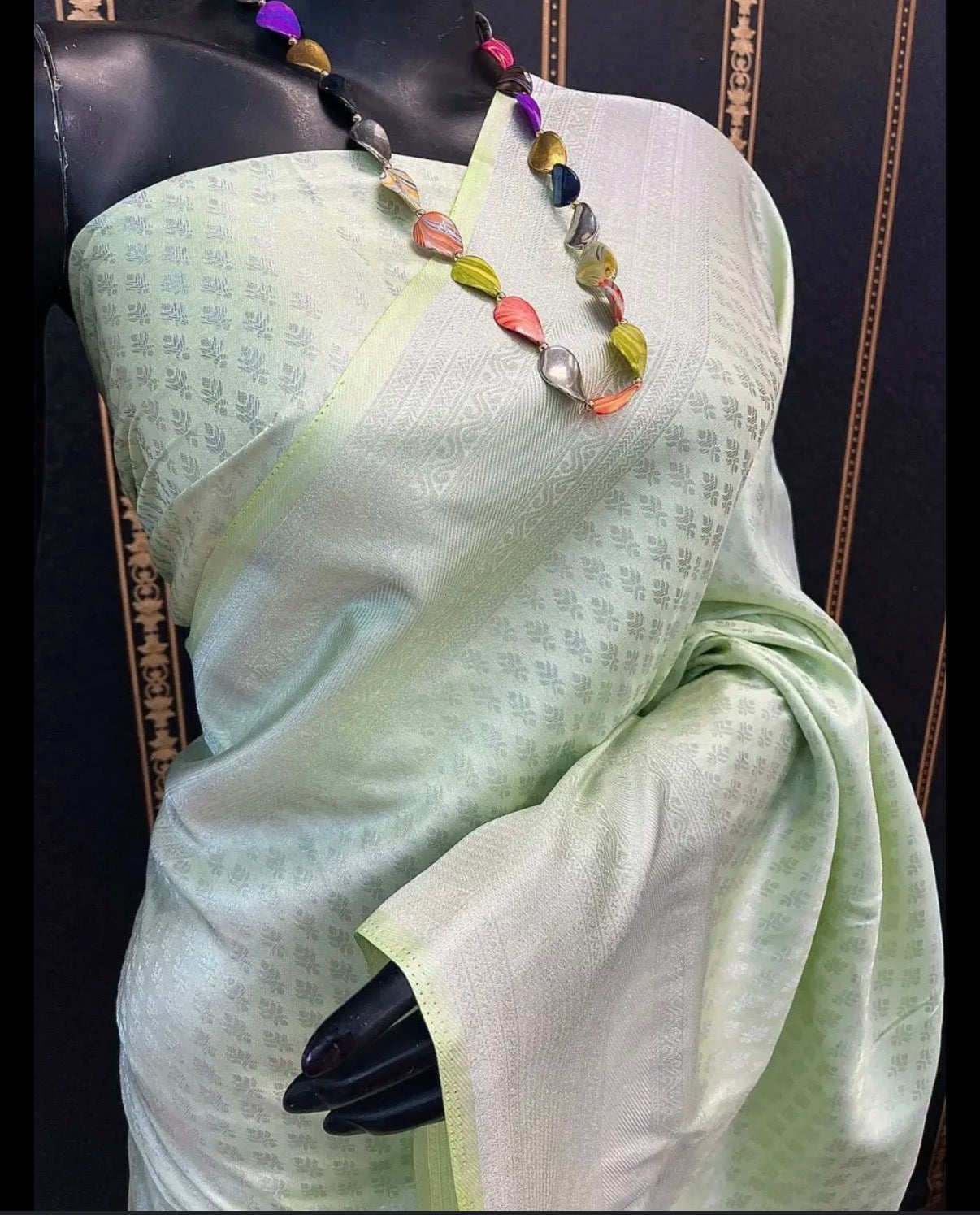 Light green saree with a colorful necklace on a mannequin against a dark background