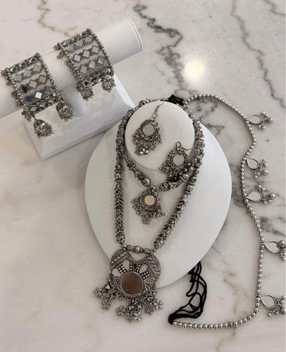 A silver-toned traditional jewelry set displayed on white mannequin stands, including a necklace with a large circular pendant, matching earrings, and a bracelet, arranged on a light marble surface.