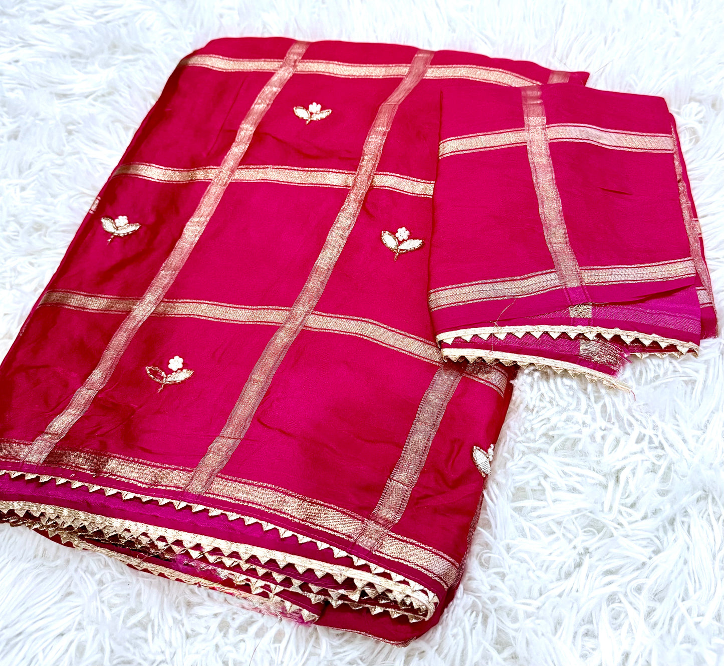 Folded pink saree with white floral patterns on a white background