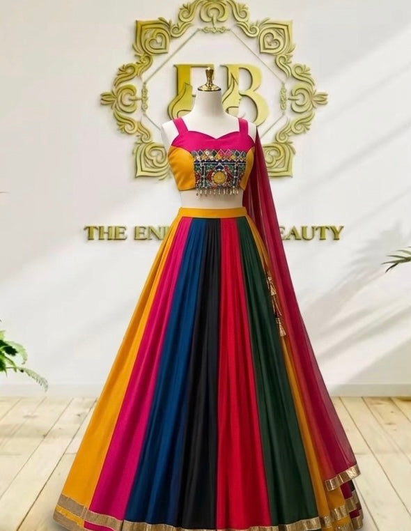 A vibrant, multicolored traditional Indian lehenga choli dress displayed on a mannequin. The dress features a bright yellow and magenta-pink choli with a heavily embroidered gold and blue center panel, a flared skirt composed of vertical stripes of yellow, magenta, blue, green, and black, and a matching sheer dupatta draped over one shoulder.