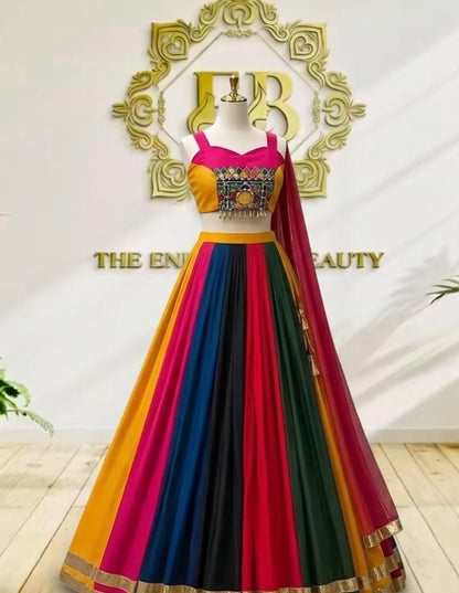 A vibrant, multicolored traditional Indian lehenga choli dress displayed on a mannequin. The dress features a bright yellow and magenta-pink choli with a heavily embroidered gold and blue center panel, a flared skirt composed of vertical stripes of yellow, magenta, blue, green, and black, and a matching sheer dupatta draped over one shoulder.