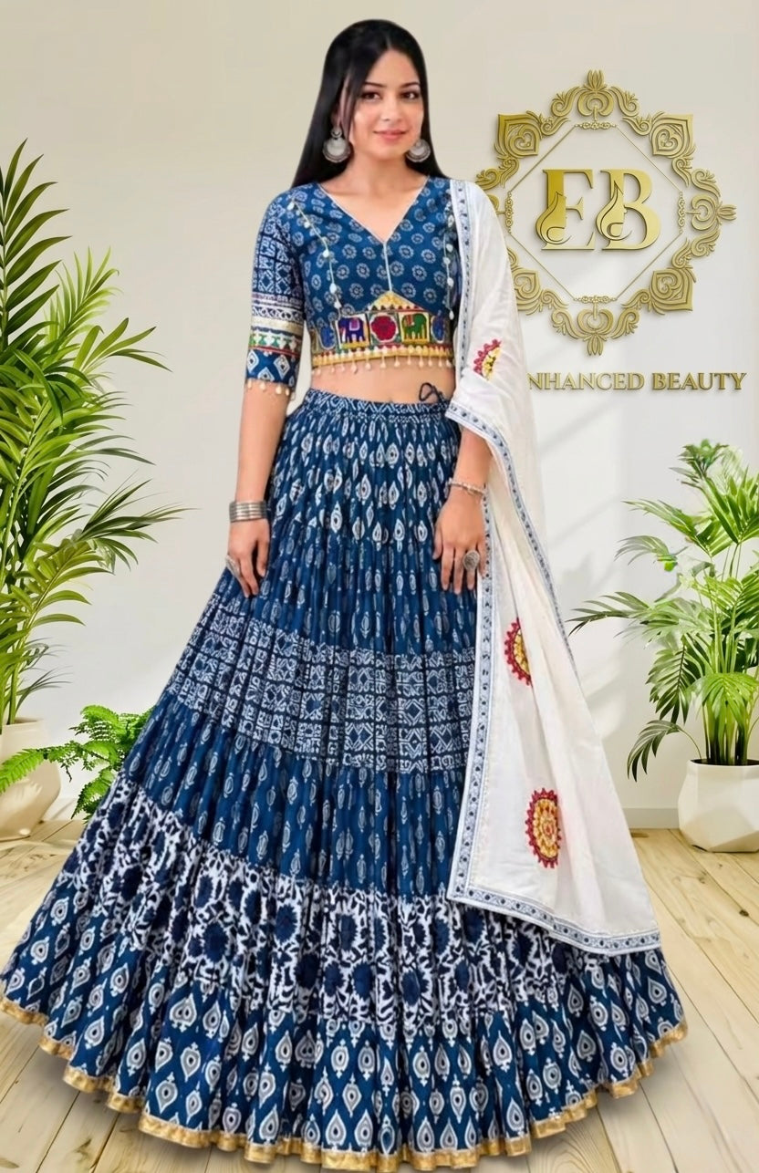 A woman models a traditional Indian lehenga choli set. The outfit features a navy blue and white printed skirt (lehenga) with a matching embroidered blouse, and a white dupatta with blue borders and red/yellow motifs.