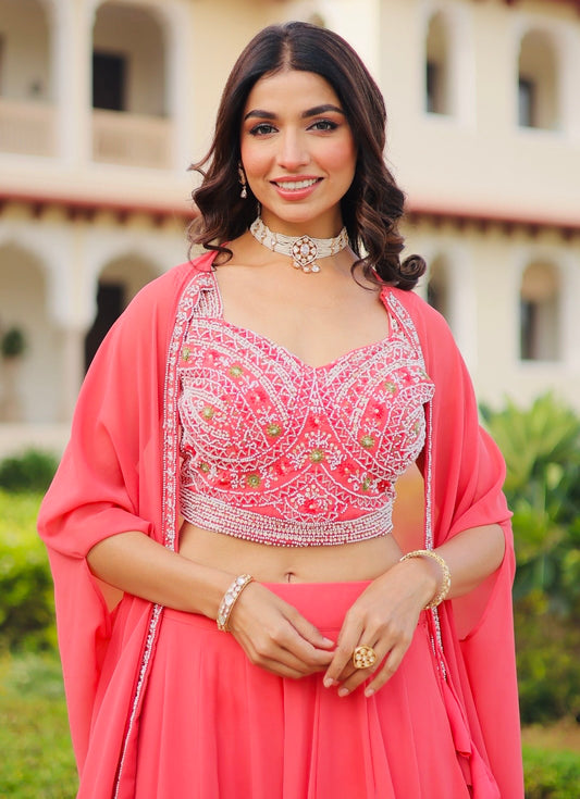 Woman in a pink traditional outfit with a decorative top and dupatta, standing outdoors.