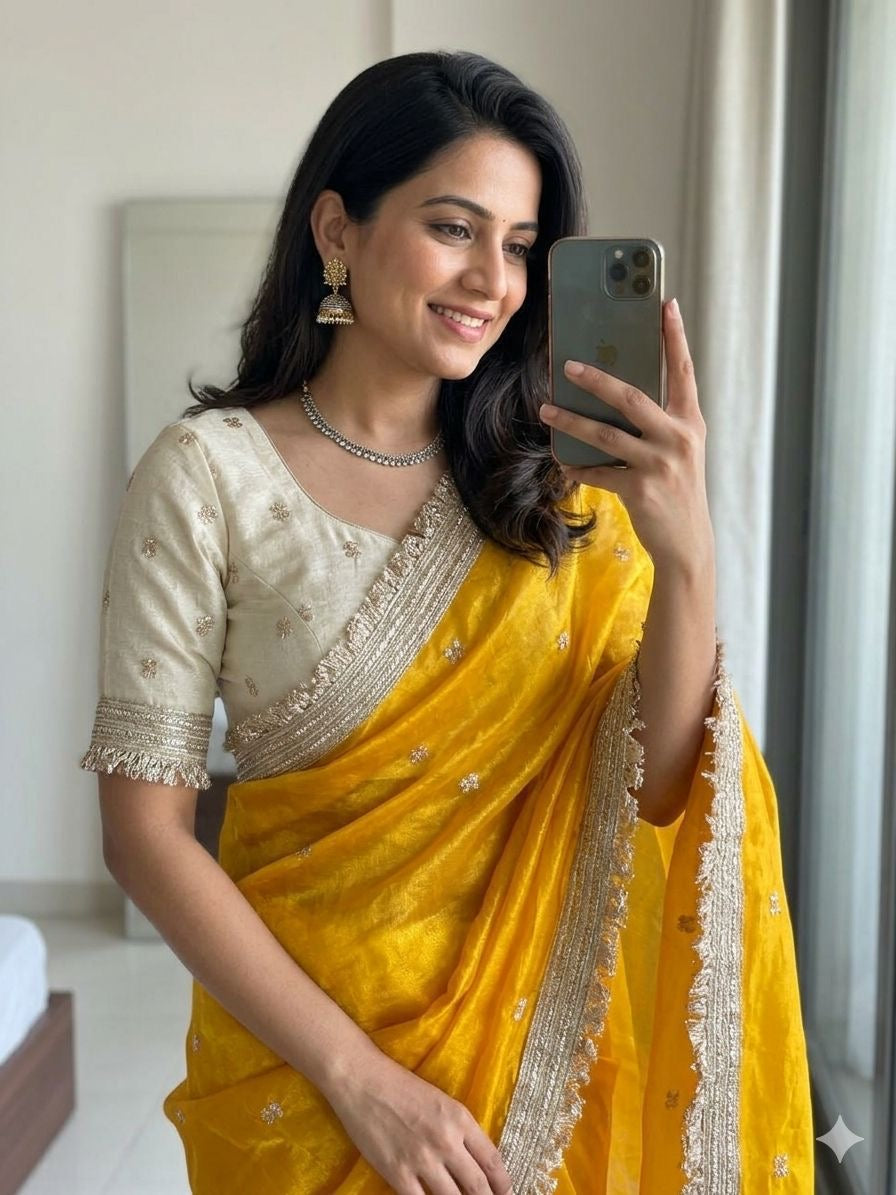 Woman in a yellow saree taking a mirror selfie.
