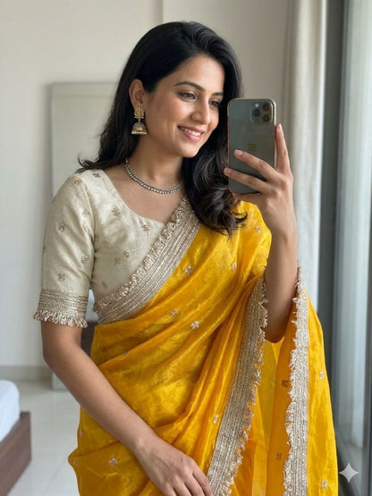 Woman in a yellow saree taking a mirror selfie.