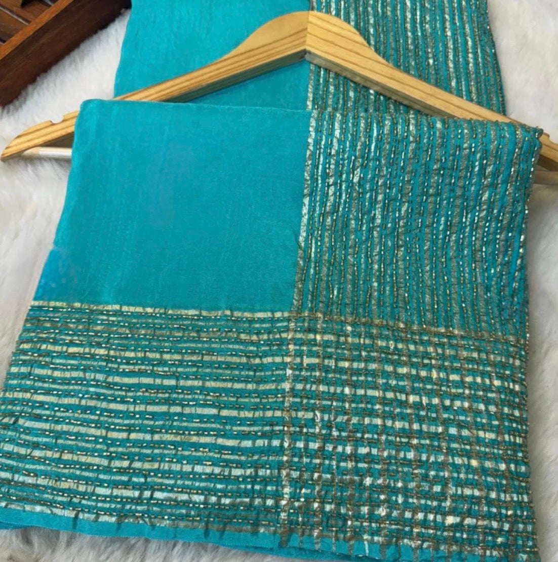 Teal fabric with gold thread pattern on a wooden hanger