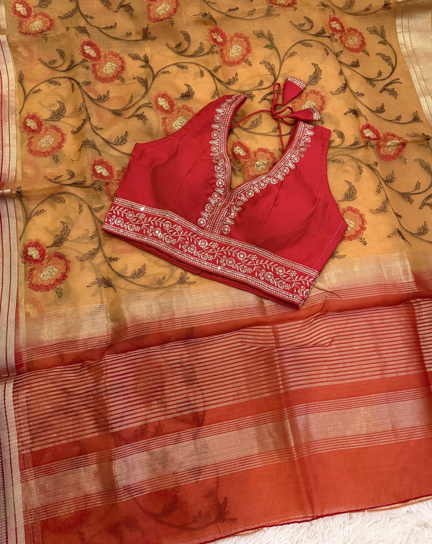 Red blouse with floral embroidery on a beige saree with red and gold patterns.