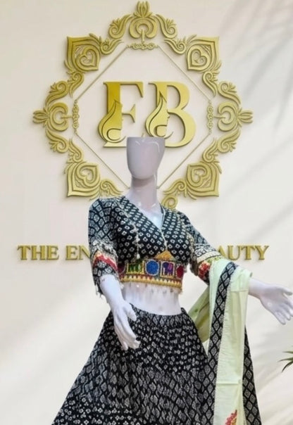 A mannequin wearing a black and white patterned traditional outfit with a light green dupatta, set against a cream-colored wall with a large gold 'FB' logo and 'THE ENCHANTMENT' text.