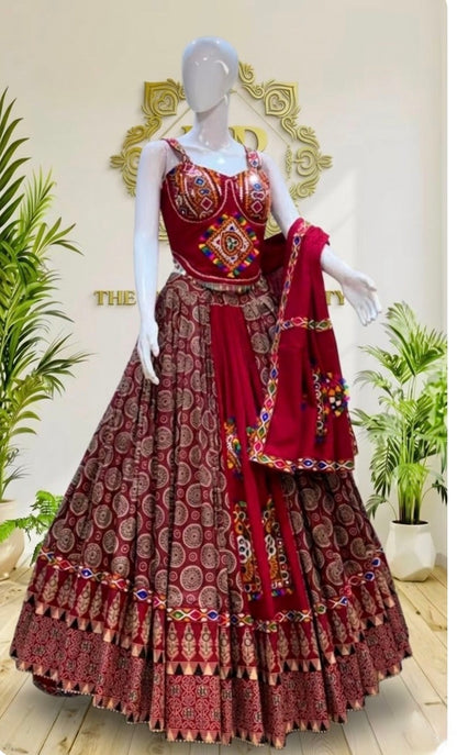A red and gold printed Indian ethnic lehenga choli set displayed on a white mannequin, featuring a heavily embroidered red choli, a flared patterned skirt, and a matching dupatta.