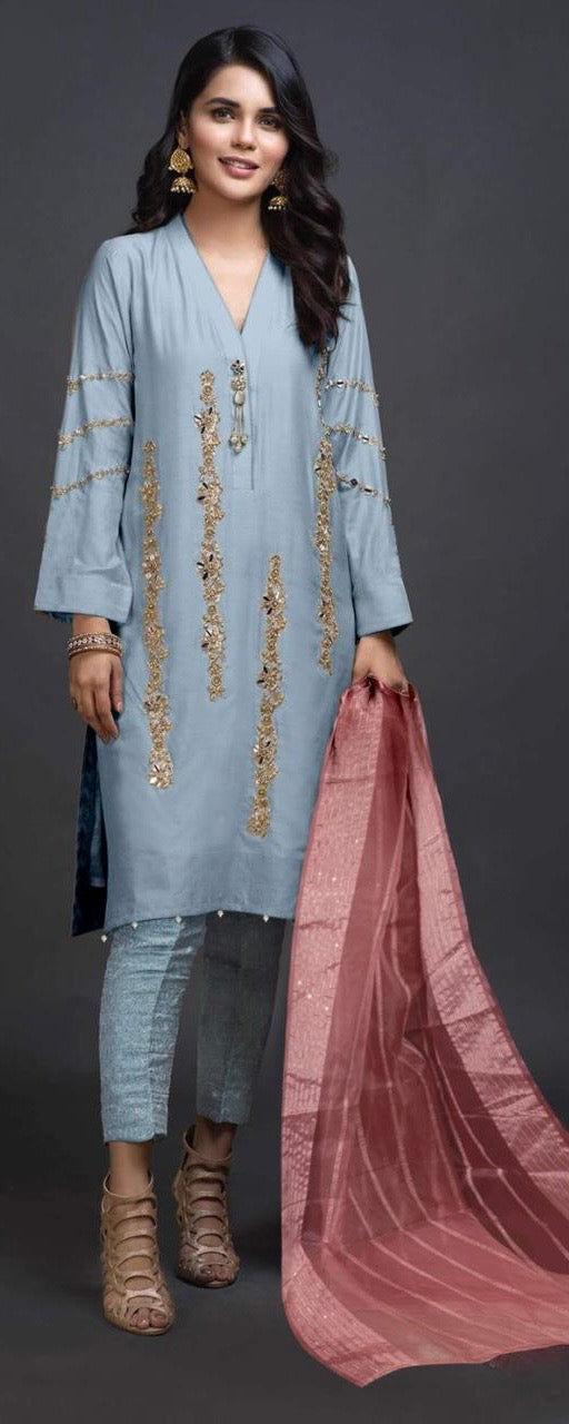 Woman wearing a light blue embroidered outfit with a pink dupatta against a dark background