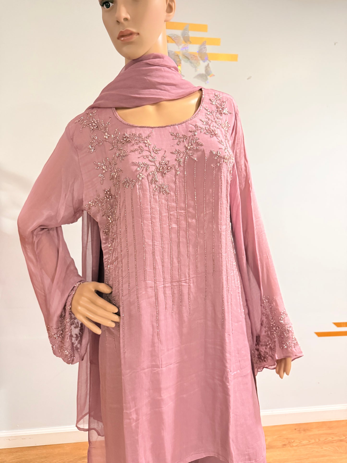 Mannequin wearing a pink dress with floral embellishments on a plain background