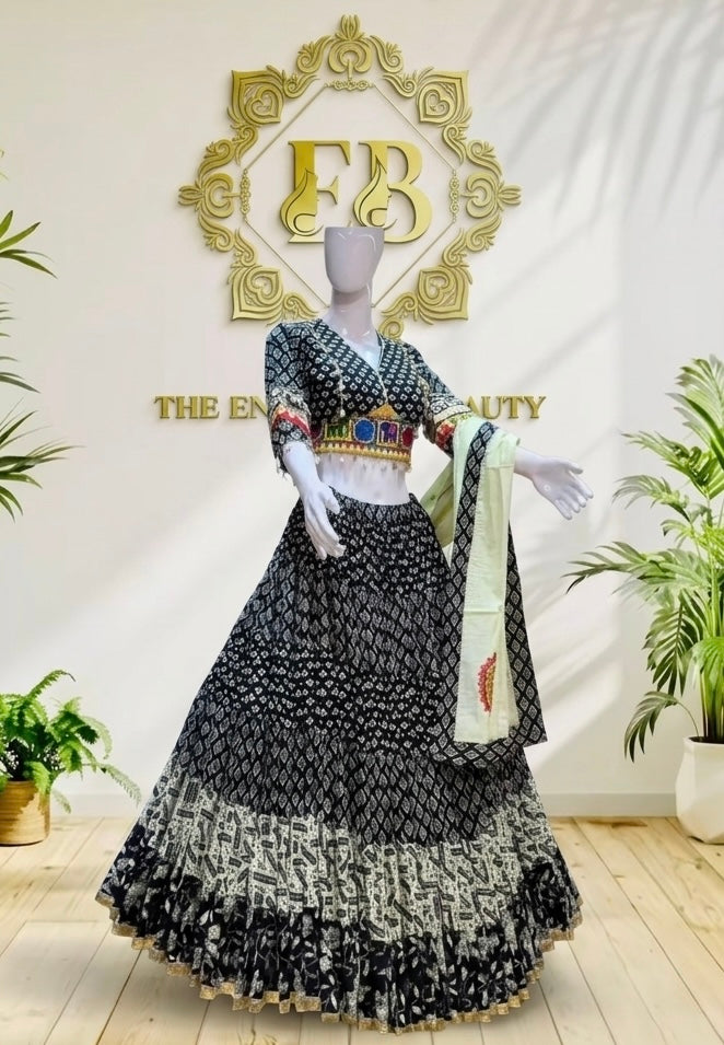 A black and white patterned Indian ethnic outfit displayed on a mannequin in an indoor showroom. The set includes a heavily embroidered black skirt with white motifs, a matching patterned blouse with gold and red embroidery, and a light green dupatta.