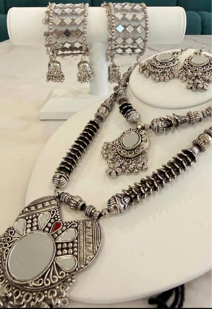 A silver-toned traditional jewelry set displayed on white mannequin stands, including a necklace with a large oval pendant, matching earrings, and two wide cuff bracelets.