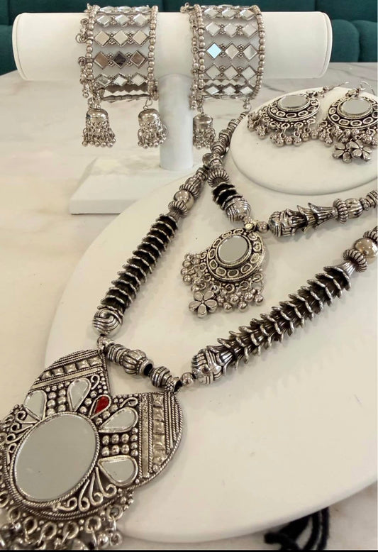 A silver-toned traditional jewelry set displayed on white mannequin stands, including a necklace with a large oval pendant, matching earrings, and two wide cuff bracelets.