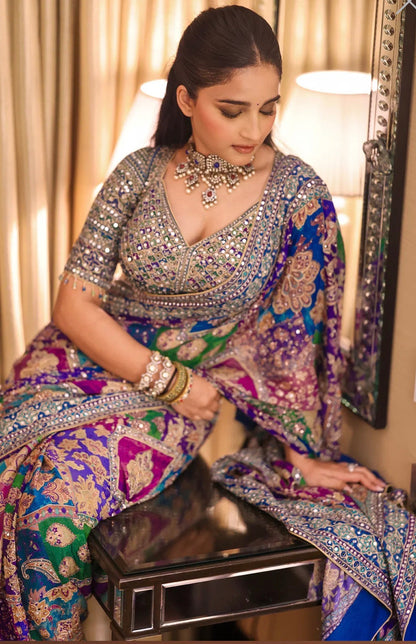 Woman in a colorful traditional outfit with intricate patterns, sitting indoors.