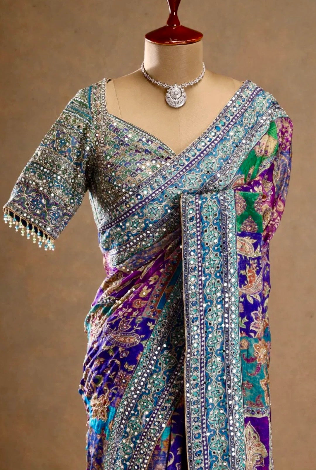 Colorful saree with intricate patterns on a mannequin against a brown background