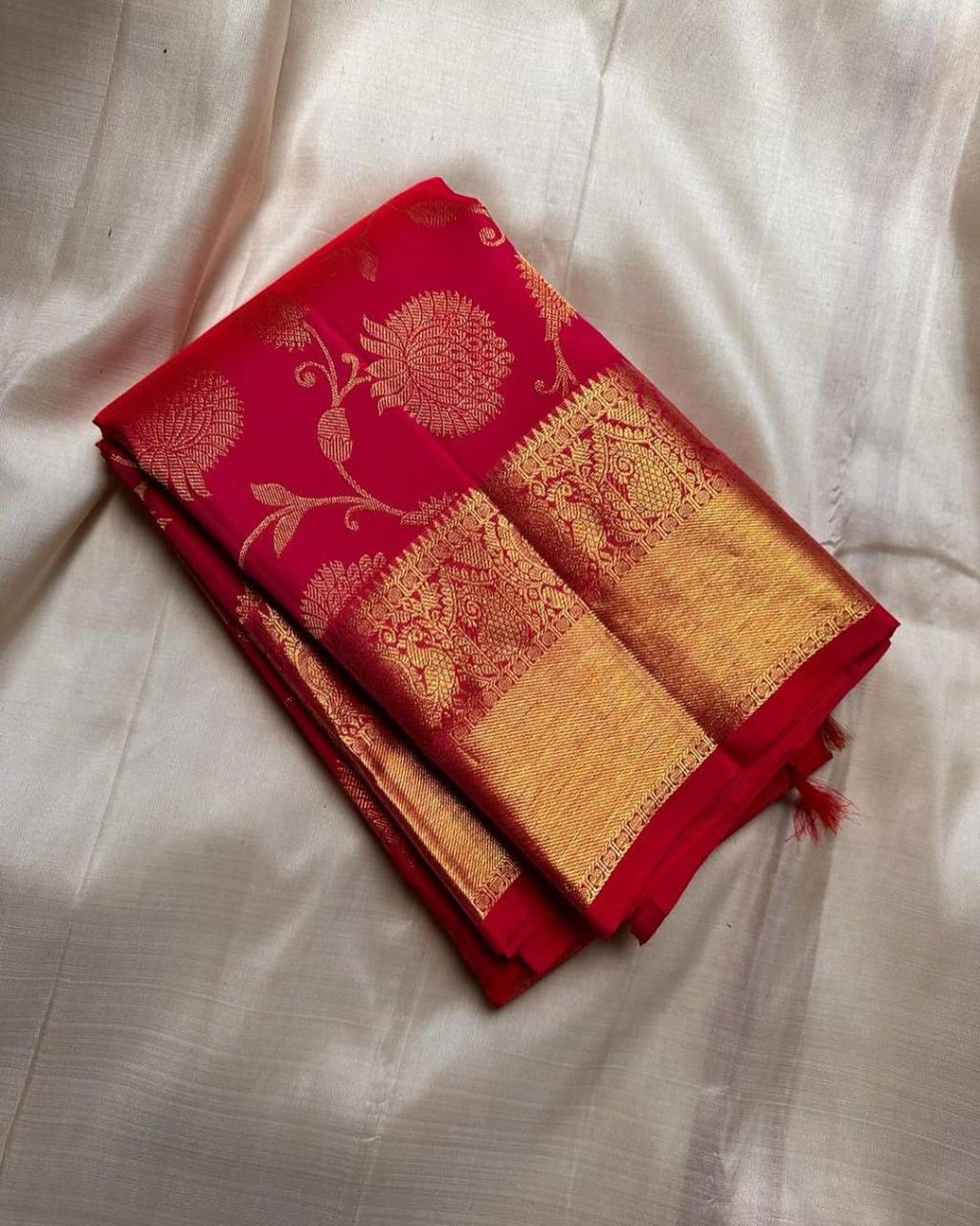 Red and gold saree with intricate patterns on a light gray fabric background