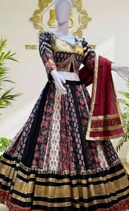 A traditional Indian lehenga choli suit displayed on a mannequin. The outfit features a black and red patterned skirt with gold zari borders, a matching embroidered choli, and a deep red dupatta with gold borders.