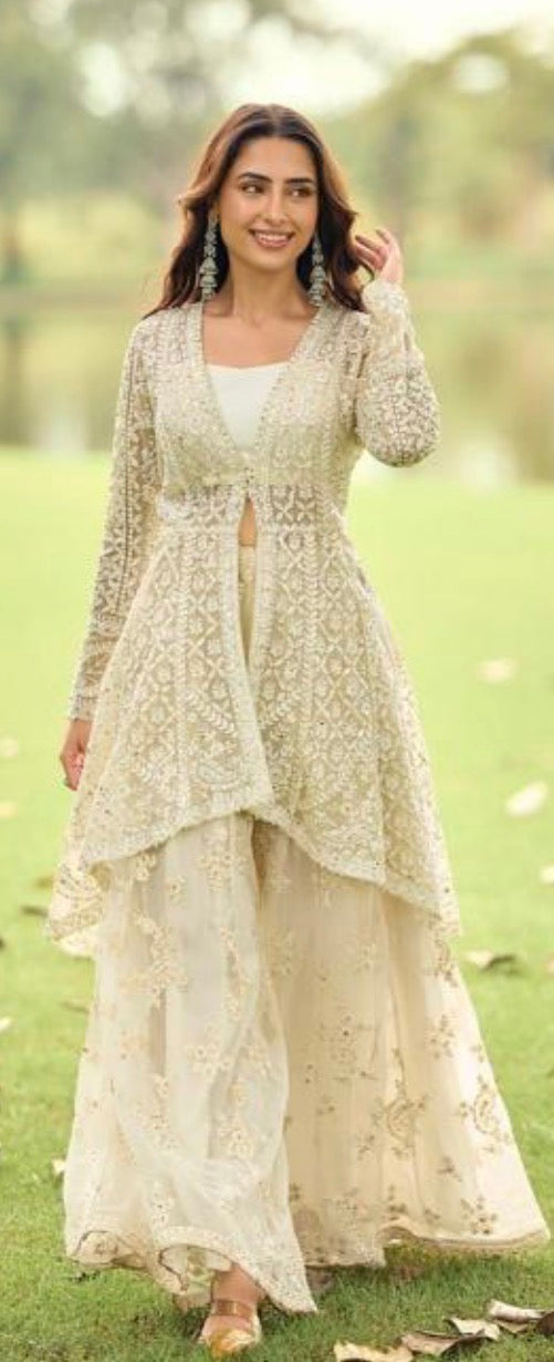 Woman in a cream-colored traditional outfit standing outdoors with greenery in the background