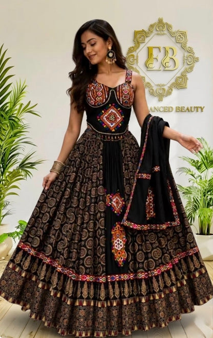 A woman models a traditional Indian ethnic wear set featuring a black and brown printed lehenga choli with intricate red and gold embroidery, paired with a black dupatta. The background is a clean indoor setting with a gold 'FB Advanced Beauty' logo and potted plants.