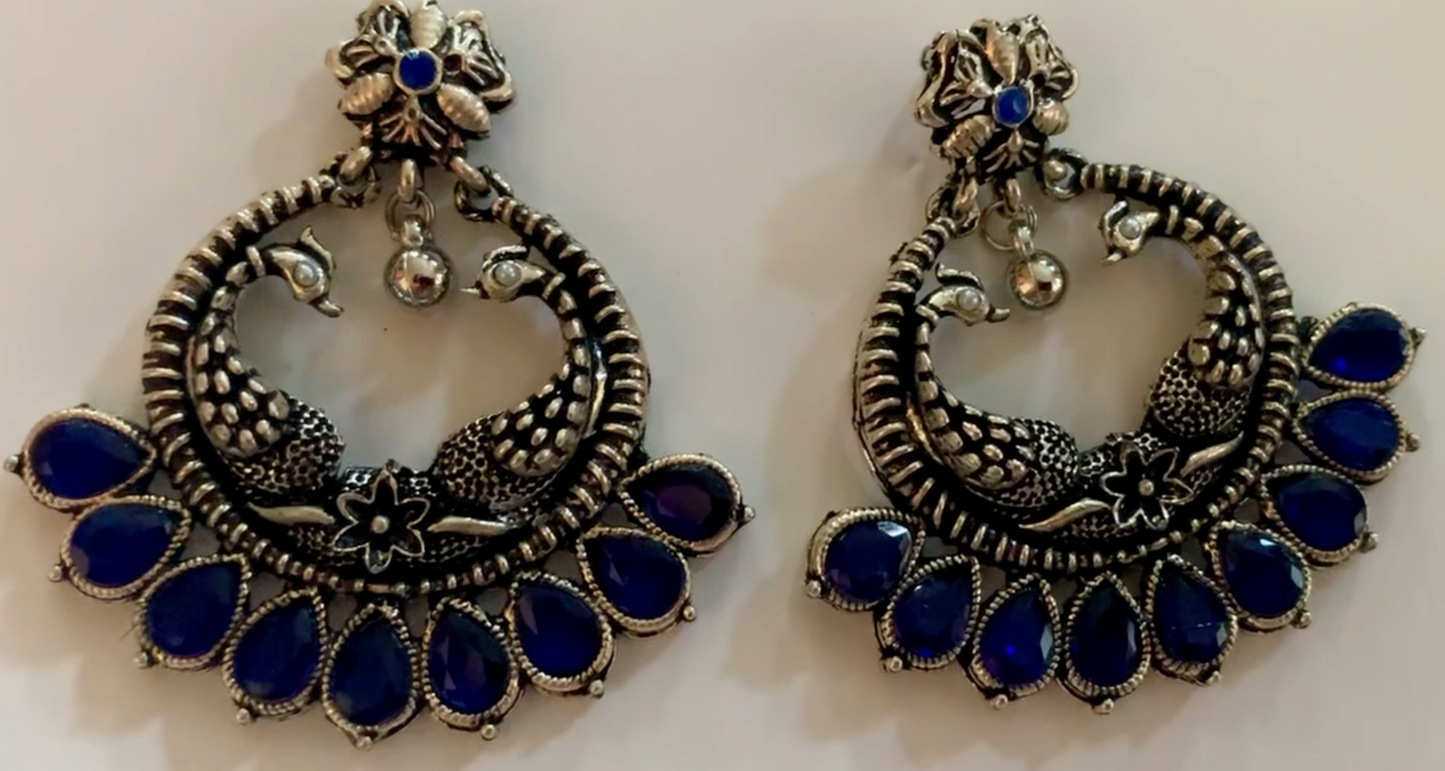 Pair of ornate earrings with blue stones on a white background