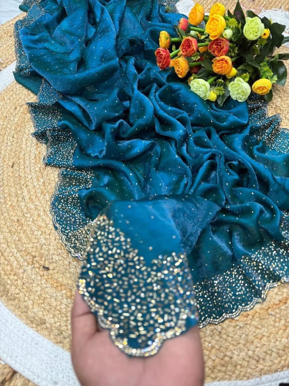 Blue decorative fabric with gold trim held by a hand, with flowers in the background.