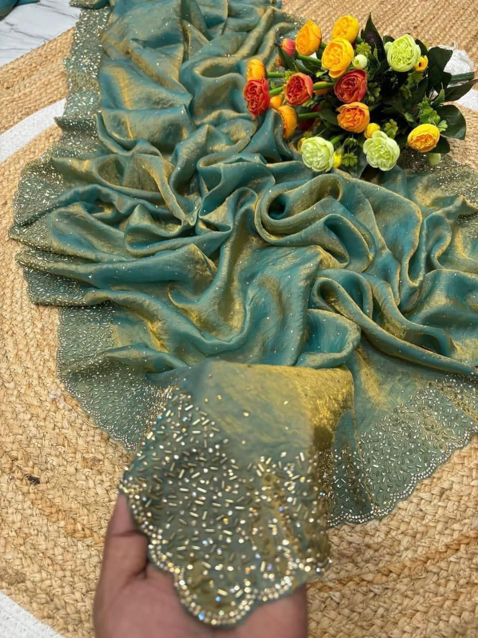 Green and gold glittery fabric with a hand holding it, and a bouquet of flowers in the background.