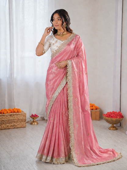 Woman wearing a pink saree with a white blouse against a white curtain background
